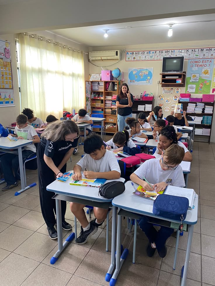 Sala de aula com alunos trabalhando em suas carteiras e duas professoras acompanhando a turma